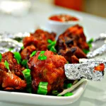 Crispy Chicken Lollipop served with spicy red sauce and garnished with spring onions.